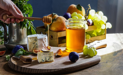 Delicious gourmet cheese Dorblu, honey, with sliced fresh figs and grapes, peaches, on a rustic wooden table