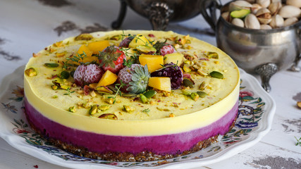 Vegan raw cheesecake with mango, black currant, blueberry, orange,  cashew cream, coconut butter and coconut milk, and base made of almonds, dates  and  dried apricots, oat flakes, lyophilisated berry