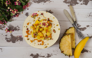 Vegan raw cheesecake with pineapple, mango, lemon and black currant cashew cream, coconut butter and coconut milk, and base made of almonds, dates  and  dried apricots, oat flakes, lyophilisated berry