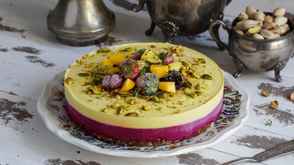 Vegan raw cheesecake with mango, black currant,  cashew cream, coconut butter and coconut milk, and base made of almonds, dates  and  dried apricots, oat flakes, lyophilisated berry