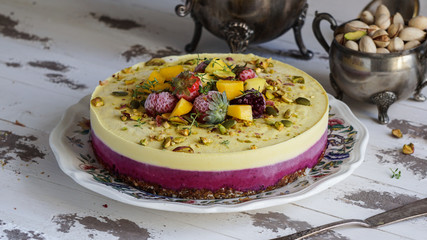Obraz na płótnie Canvas Vegan raw cheesecake with mango, black currant, cashew cream, coconut butter and coconut milk, and base made of almonds, dates and dried apricots, oat flakes, lyophilisated berry