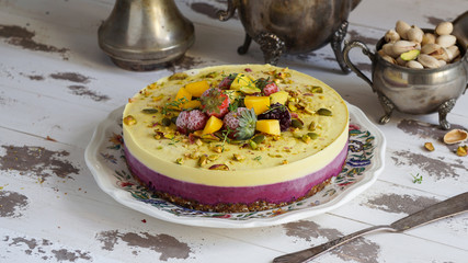 Vegan raw cheesecake with mango, black currant,  cashew cream, coconut butter and coconut milk, and base made of almonds, dates  and  dried apricots, oat flakes, lyophilisated berry