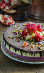Vegan raw cheesecake with black currant, mango,  chocolate,  cashew cream, coconut butter and coconut milk, and base made of almonds, dates  