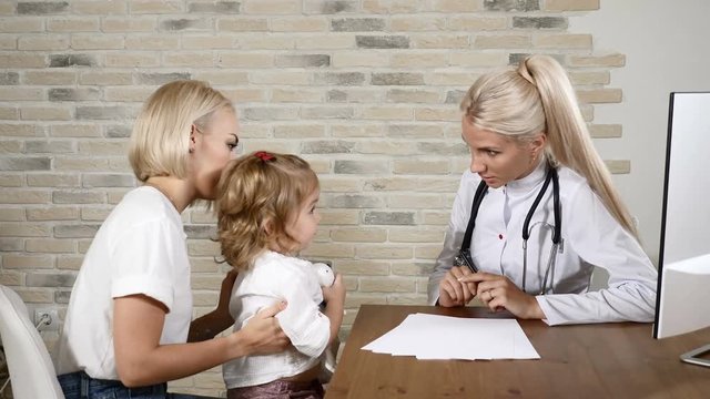 Young female pediatrician making friends with a little pretty girl and her mom in healthcare clinic. Friendly medicine concept. 4k