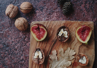 Fresh organic figs, nuts and autumn leaves on wooden board and dark stone table. Healthy lifestyle, seasonal fruit, sweet dessert, top view, selective focus