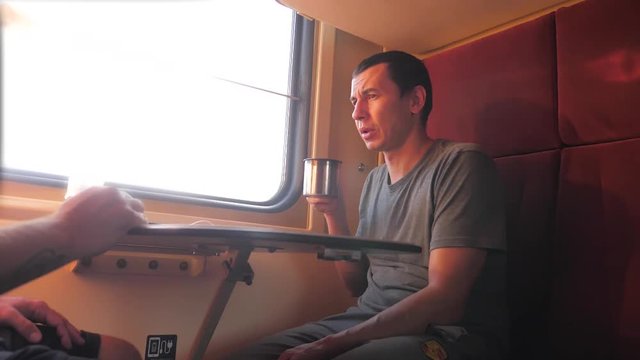 man is sitting on the train carriage holding a Railway and drinking coffee and tea. slow motion video. two men drinking tea on the train talking lifestyle the train social media . man with smartphones