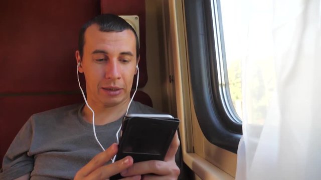 man listening to the music on the train rail car coupe compartment travel. slow motion video. man with a smartphone at the window of a train in a car travel internet social media web. lifestyle man
