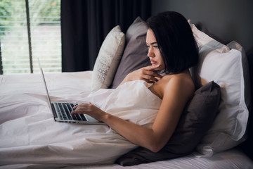 Fototapeta premium Young beautiful caucasian woman laying on bed and using laptop to work after wake up and thinking about work. Copy space