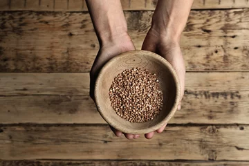 Plexiglas foto achterwand Poor woman holding bowl with grains against wooden background, closeup © New Africa