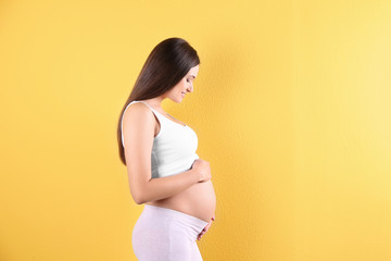 Beautiful pregnant woman holding hands on belly against color background. Space for text