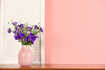 Beautiful bouquet of purple eustoma flowers in vase near color wall with space for text