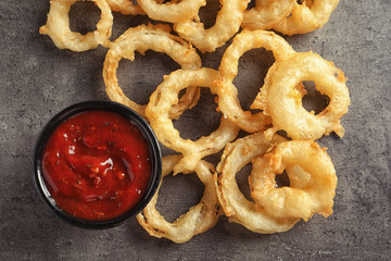 Delicious golden crispy onion rings and sauce on gray background, top view