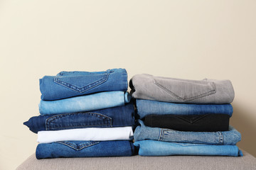 Stack of different jeans on ottoman against light background