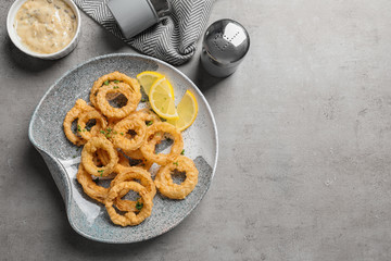Homemade crunchy fried onion rings and sauce on gray background, top view. Space for text