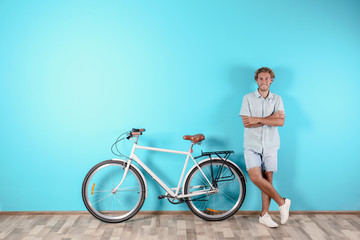 Handsome man with bicycle against color wall. Space for text