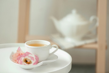 Cup of tea, saucer and flowers on table indoors
