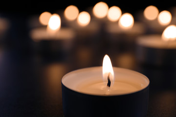 Burning candle on table in darkness, closeup. Funeral symbol