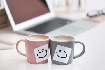 Coffee cups with cute stickers on table at modern workplace