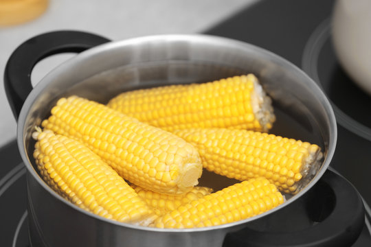 Stewpot with water and corn cobs on stove, closeup