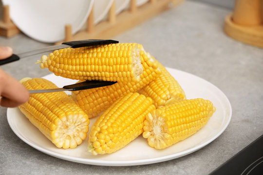 Taking corn cob from plate with tongs, closeup