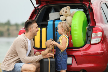 Father and daughter near car trunk with suitcases outdoors