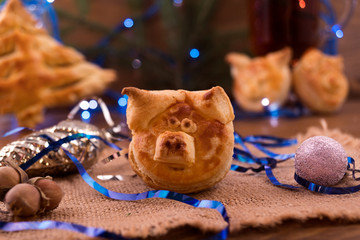 Homemade puff pastry in the shape of a pig's head – the symbol of 2019, next to a linen napkin Christmas toys and decorations.