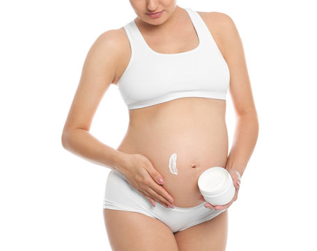 Pregnant woman applying body cream on belly against white background, closeup