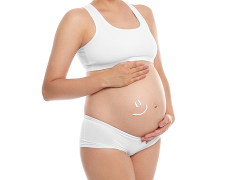 Smile painted with body cream on pregnant woman's belly against white background, closeup