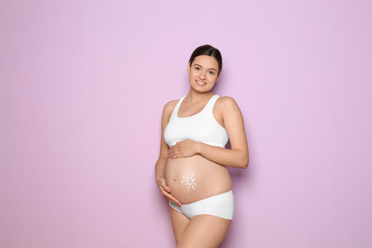 Sun painted with body cream on pregnant woman's belly against color background