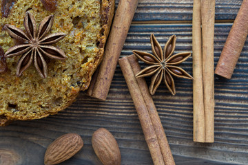 Autumn pumpkin spice. Homemade spicy pumpkin cake slices with walnuts, brown sugar, anise stars, raisins, cinnamon on rustic wooden brown background. Autumn mood tasty dessert, top view. Copy space.
