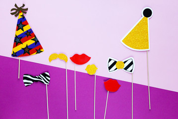 Fototapeta na wymiar creative decoration for birthday party - photo booth with hats, lips, bows on the sticks on bright pink and violet background. Happy birthday celebration concept. flat lay, copyspace