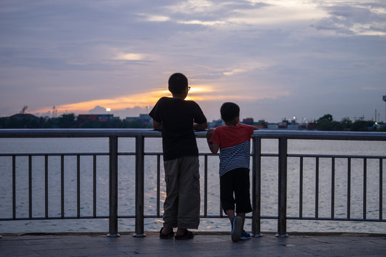Silhouette photo of Two Small children standing at railing looking to the sea while sunset.