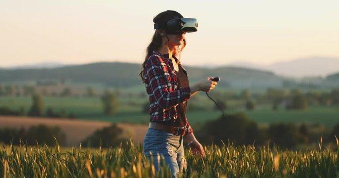 Woman Using Virtual Reality Glasses Outdoors. SLOW MOTION 4K. Young female playing in VR headset, touching virtual objects while standing in the field. Virtual reality world concept. 