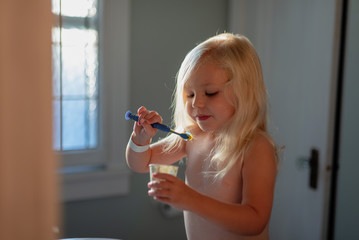 Little blonde girl brushing teeth in the morning