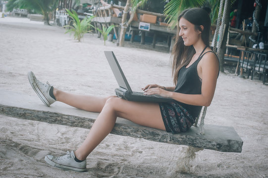 Happy woman with laptop enjoying in swing on tropical beach
