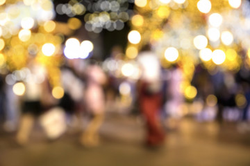 Blurry background image of defocused outdoor Christmas decorations with colorful lights and people in busy city street at night