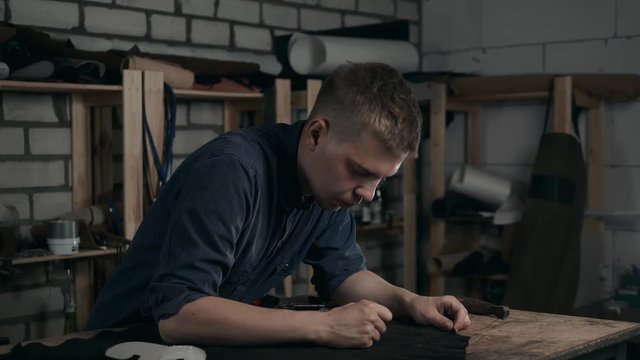 Close up of a shoemaker man working with leather using crafting tools in diy boots production close up