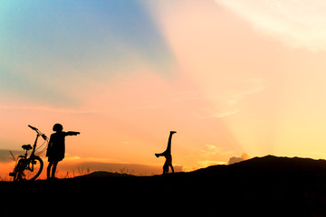 Happy children playing upside down outdoors in summer park walking on hands at sunset