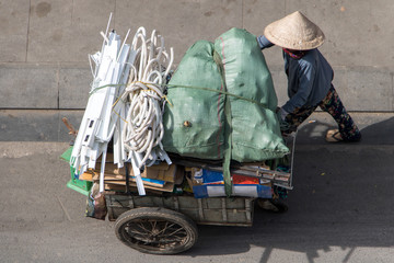 Collection of recyclable waste in the streets of Ho Chi Minh city. Vietnamese woman pushing a cart...
