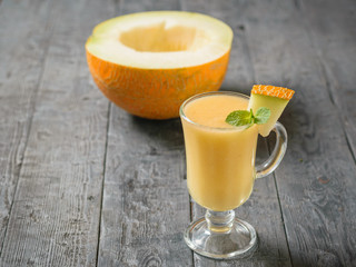 Glass mug with melon smoothie and a half melon on a wooden table.