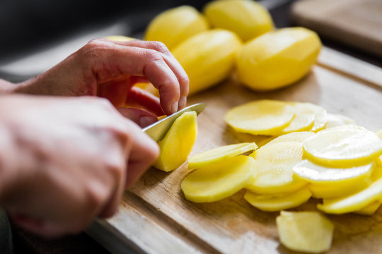 Mann beim Schneiden von Kartoffeln, Kartoffelscheiben auf dem Holzbrett
