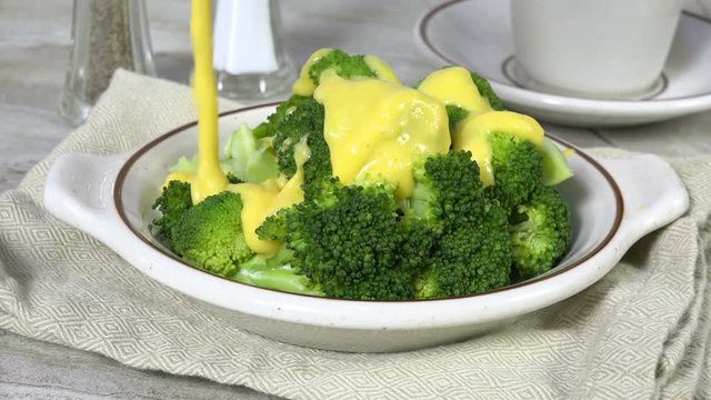 Pouring creamy cheese sauce onto broccoli