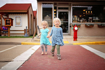 Two little Toddler Girls Holding Hands Crossing the Road on a small Town Main Street