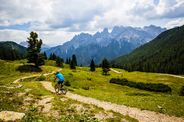 Fototapeta na wymiar Tourist cycling in Cortina d'Ampezzo, stunning rocky mountains on the background. Man riding MTB enduro flow trail. South Tyrol province of Italy, Dolomites.