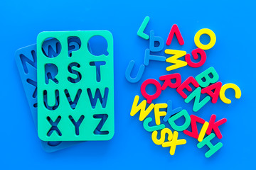 Alphabet for kids concept. English letters in disorder near stencil on blue background top view