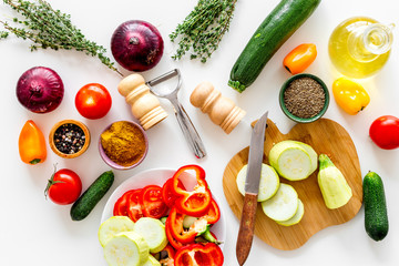 Cooking vegetable stew concept. Fresh vegetables squash, bell pepper, tomato, spices and cutting doard on white background top view