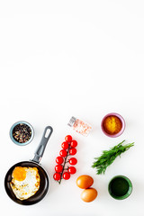 Cooking, preparing fried eggs with vegetables. Ready eggs in a frying pan near cherry tomatoes, greenery, spices, raw eggs on white background top view copy space