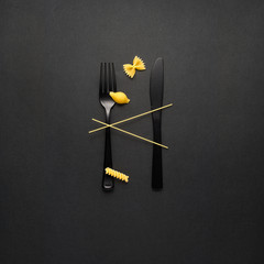 Tasty pasta / Creative still life photo of fork and spoon with raw pasta on black background.