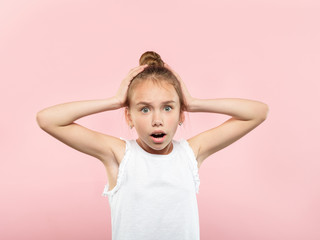 omg unbelievable shock amazement. dumbfounded child clutching her head with hands. portrait of a young girl on pink background. emotion facial expression and reaction concept.