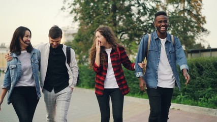 Slow motion of happy friends tourists walking in the street smiling and talking then doing high-five on summer day. People, relationship and youth concept. - Powered by Adobe